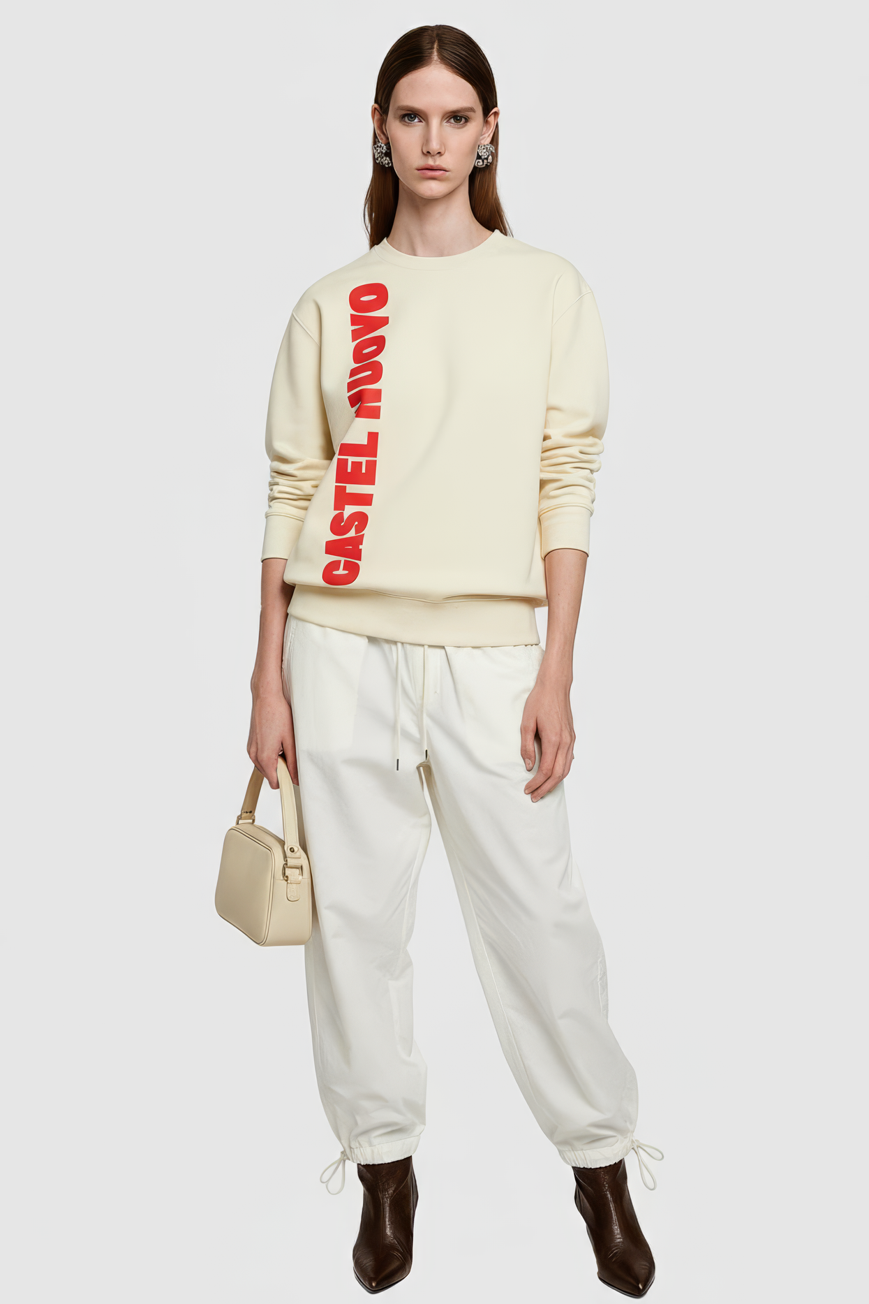 Woman wearing a cream sweater with red text and white pants on a white background
